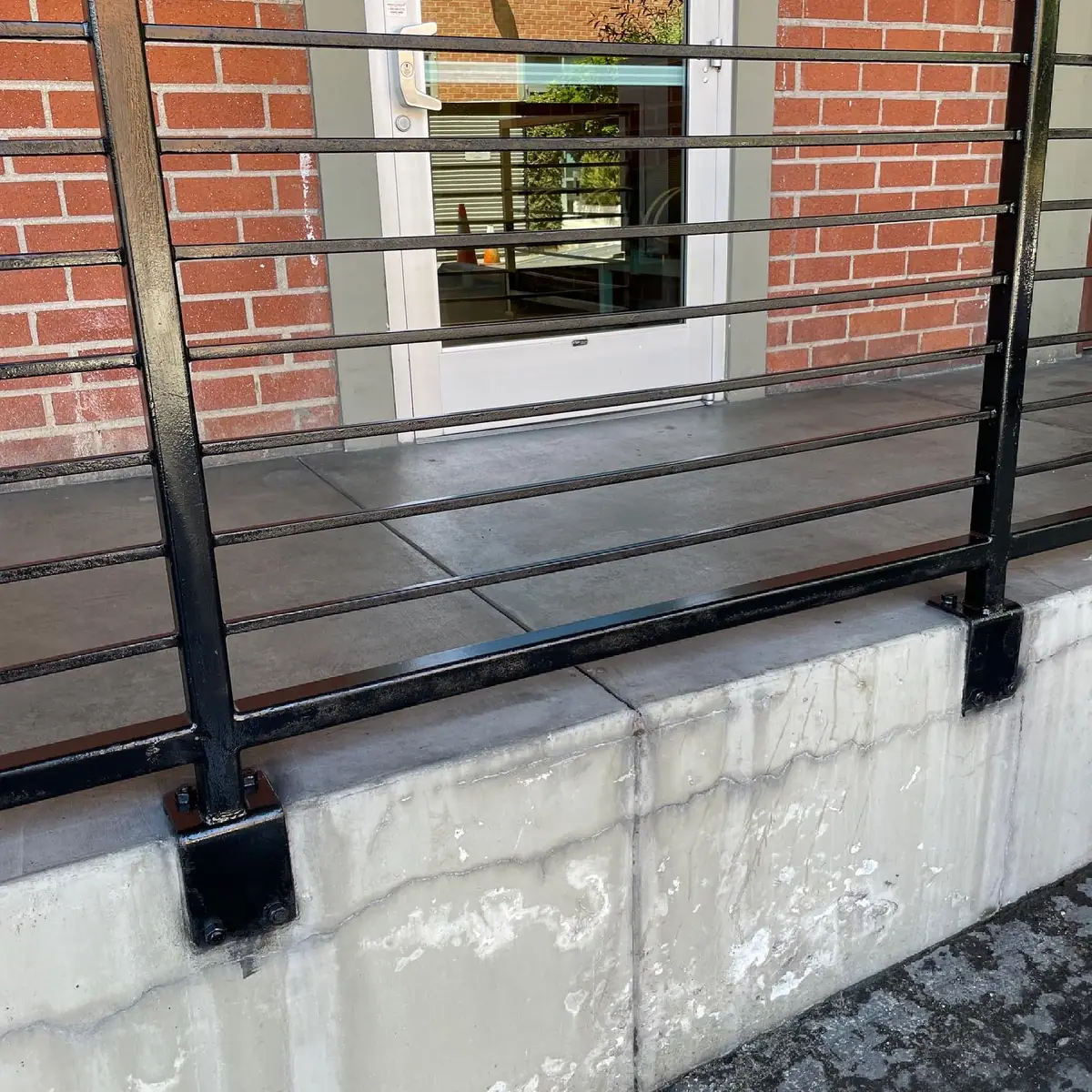 Metal railing repainted black above a stained concrete planter wall